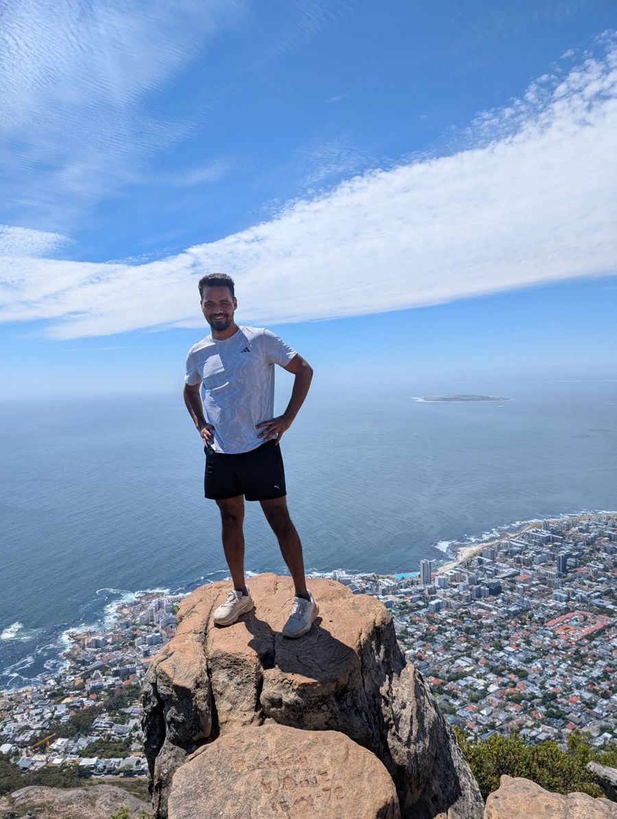 Abhishek standing on a rock at the top of a hike, ocean and city below
